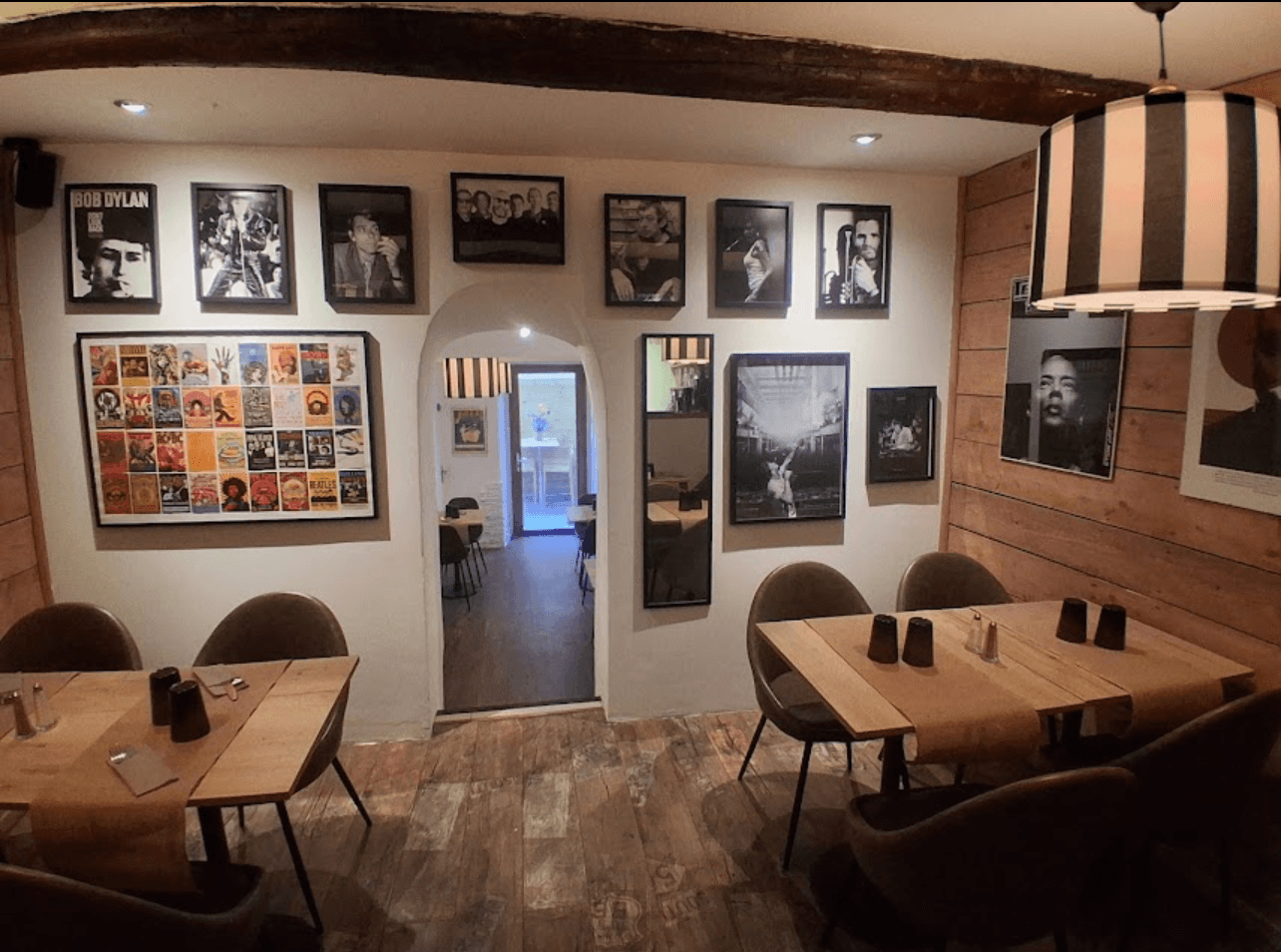 La salle du Resto des Artistes : poutres apparentes, mur de portraits de musiciens en noir et blanc, collage d'affiches de concerts, abat-jour rayé et arche blanche vers la terrasse